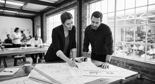 Two colleagues reviewing plans by a window